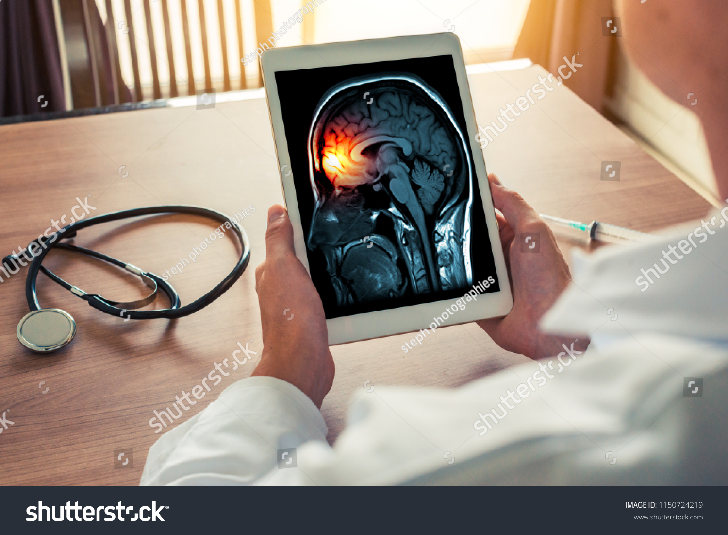 Doctor holding a digital tablet with x-ray of brain and skull skeleton. Headache, meningitis and migraine concept with stethoscope and syringe on the desk #1150724219