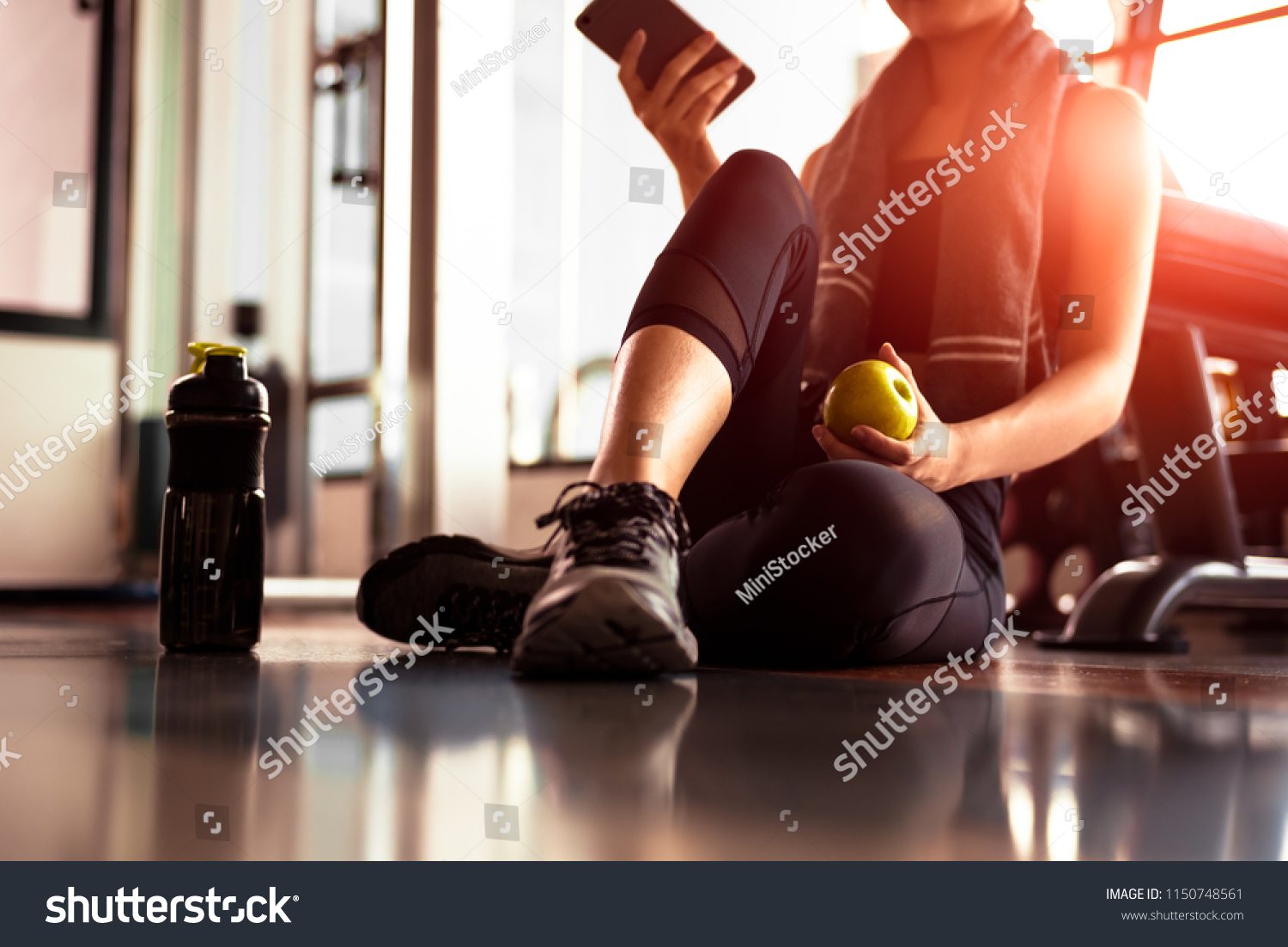 Close up of woman using smart phone and holding apple while workout in fitness gym. Sport and Technology concept. Lifestyles and Healthcare theme. #1150748561