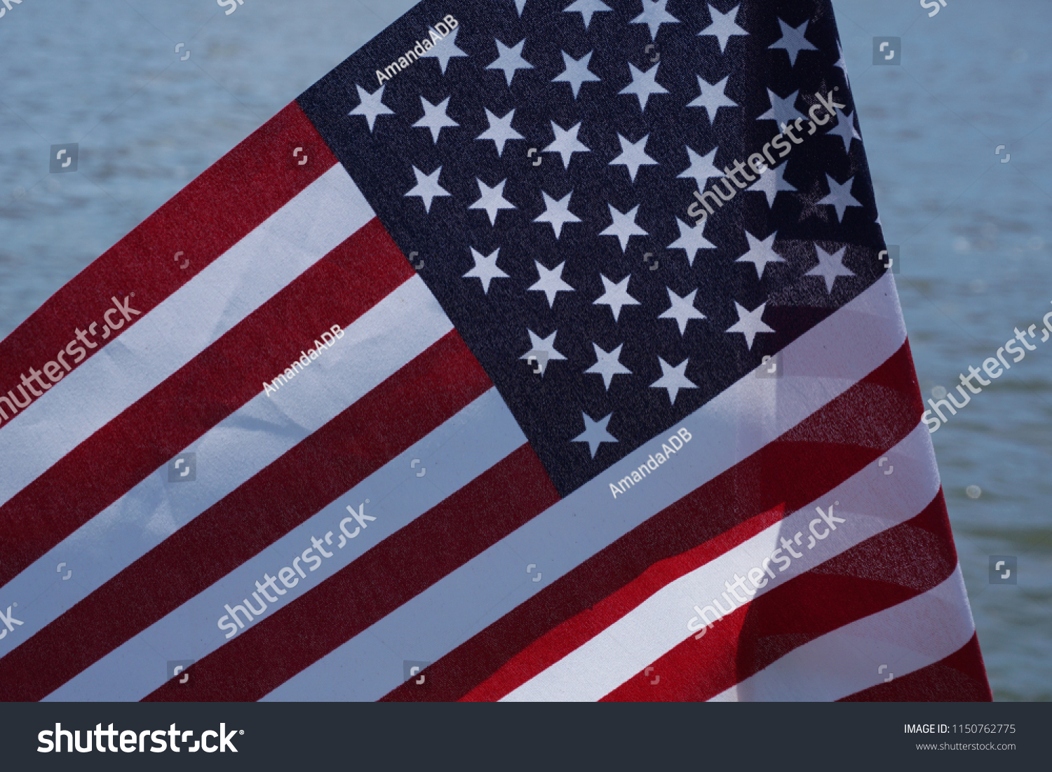 A nice United States flag with rich red and blue Stars and Stripes folded in the wind up close with a lake background.  Water from USA lake while patriots celebrate America on a summer day with symbol #1150762775