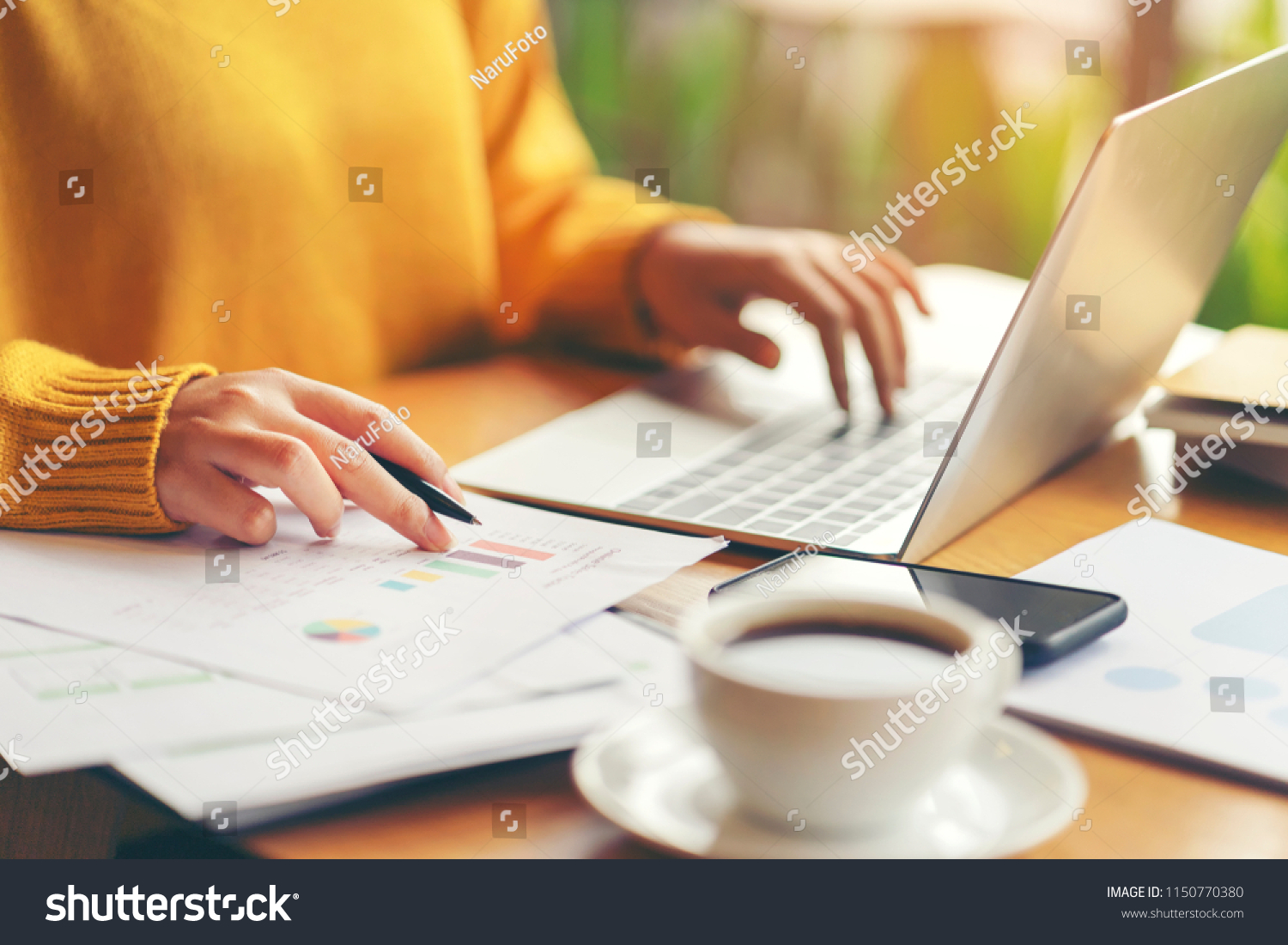 Young serious accountant woman checking paperwork from accounting department to analyse number on document, using laptop check business database, information comparing. Typing keyboard for recording #1150770380