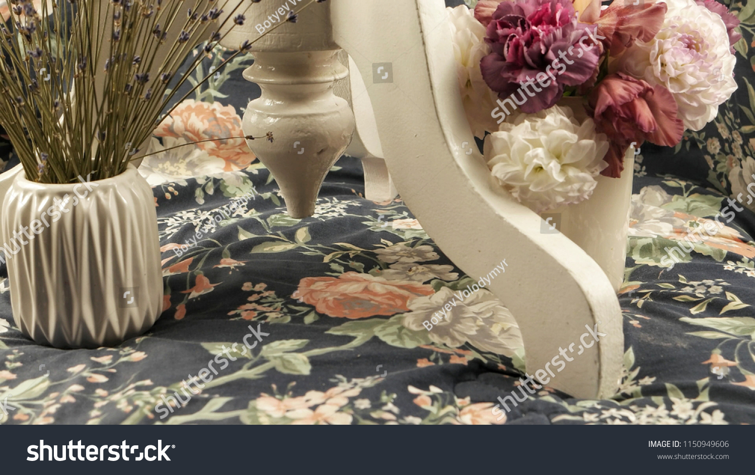 A leg of a white wooden table and a vase with flowers on a fabric with a floral pattern, a floral arrangement. #1150949606
