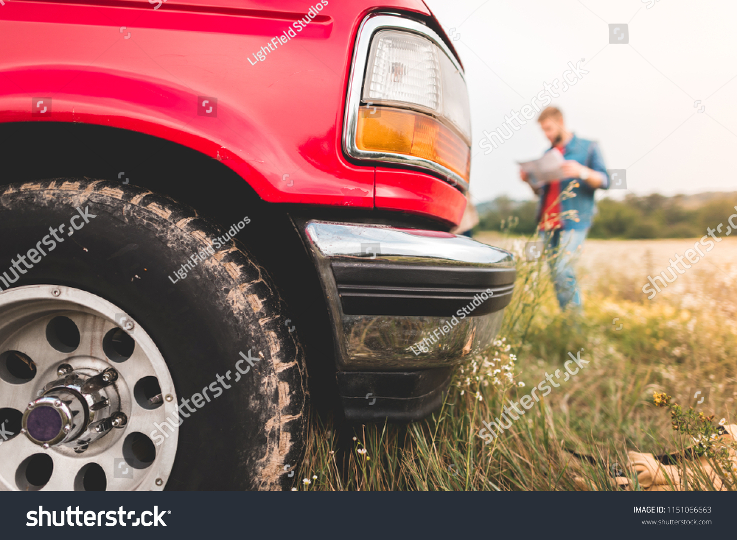 close-up shot of red truck standing in field with blurred man navigating with map on background #1151066663