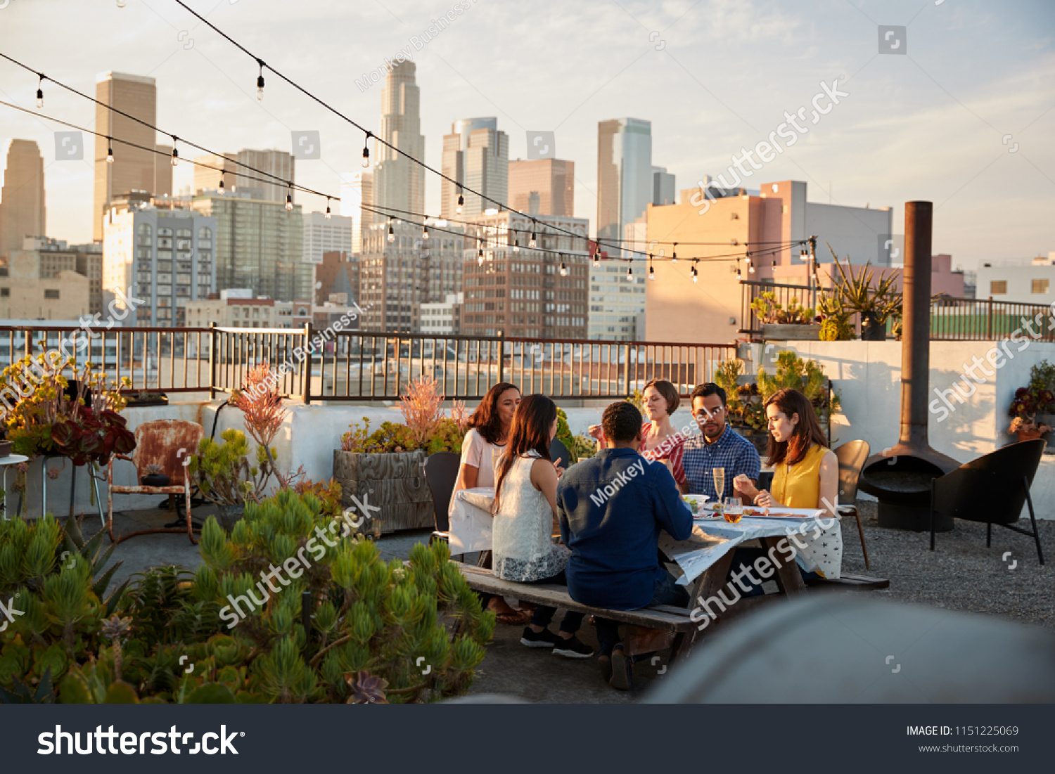 Friends Gathered On Rooftop Terrace For Meal With City Skyline In Background #1151225069