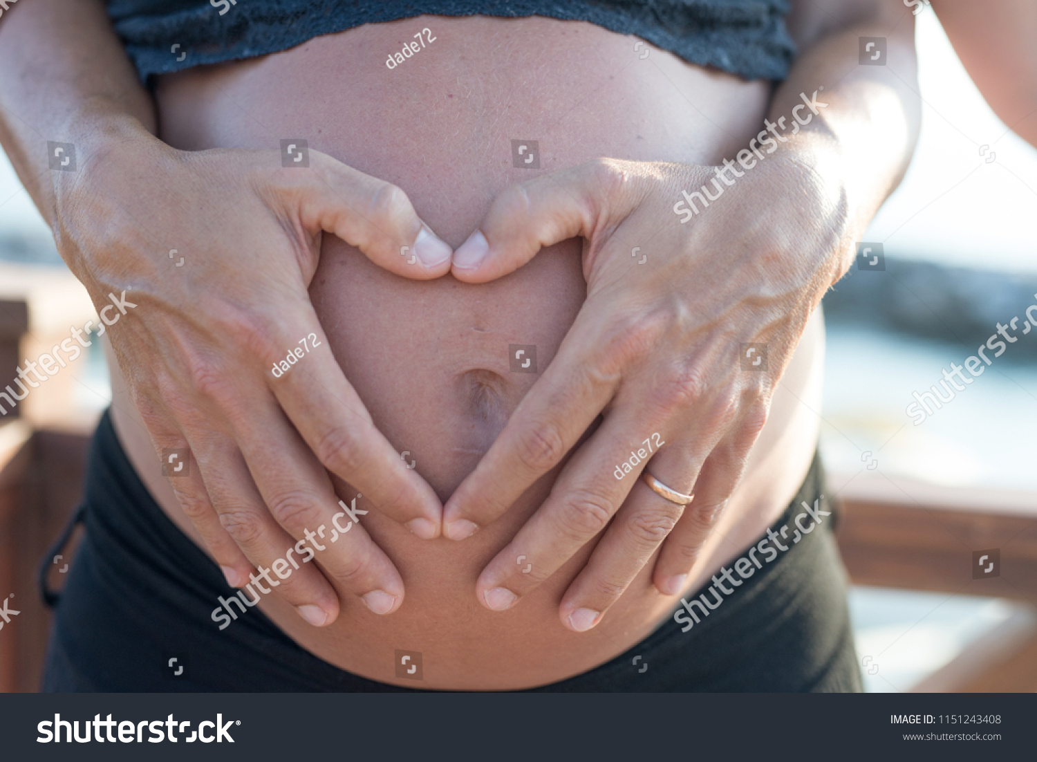Pregnant woman on the beach - hands of the husband in heart shape on belly. #1151243408