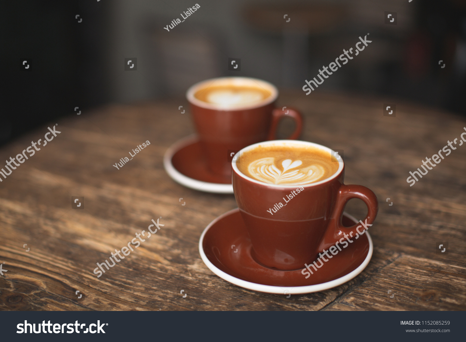 Two beautiful burgundy cups of cappuccino with trendy heart shape latte art. Summer loft cafe background. Urban space. Drinking coffee on the terrace. #1152085259