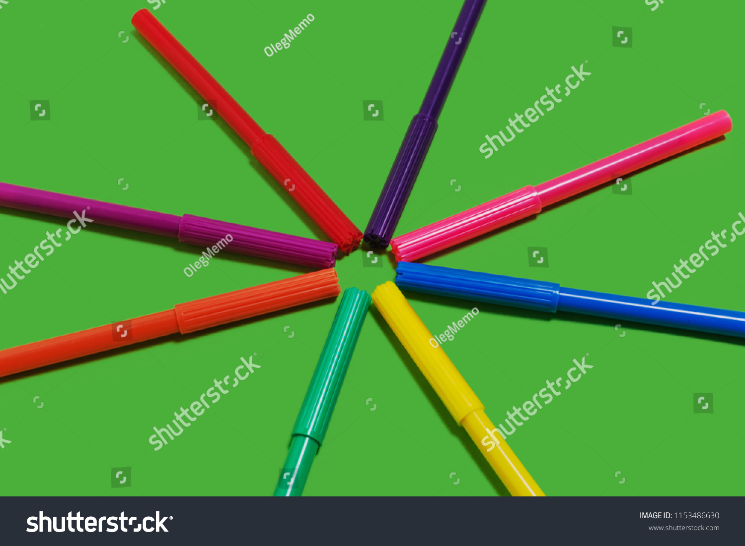 collection of new bright plastic colored felt pens lying cap to cap forming a circle on a green background. concept of office supplies #1153486630