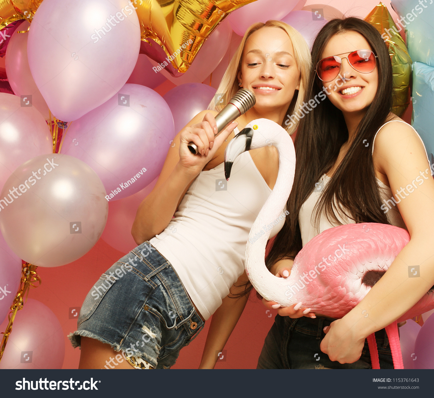lifestyle, party  and people concept: Happy young girls with microphone and flamingo over вackground of  colorful balloons  #1153761643