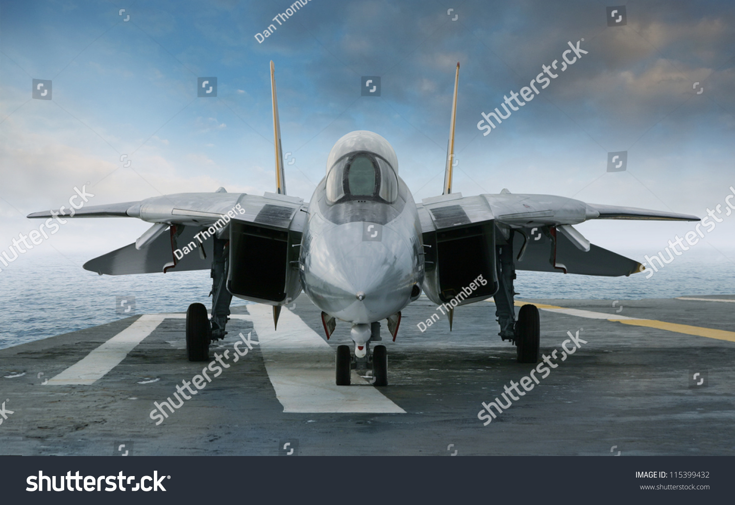 An F-14 jet fighter on an aircraft carrier deck beneath blue sky and clouds viewed from front #115399432