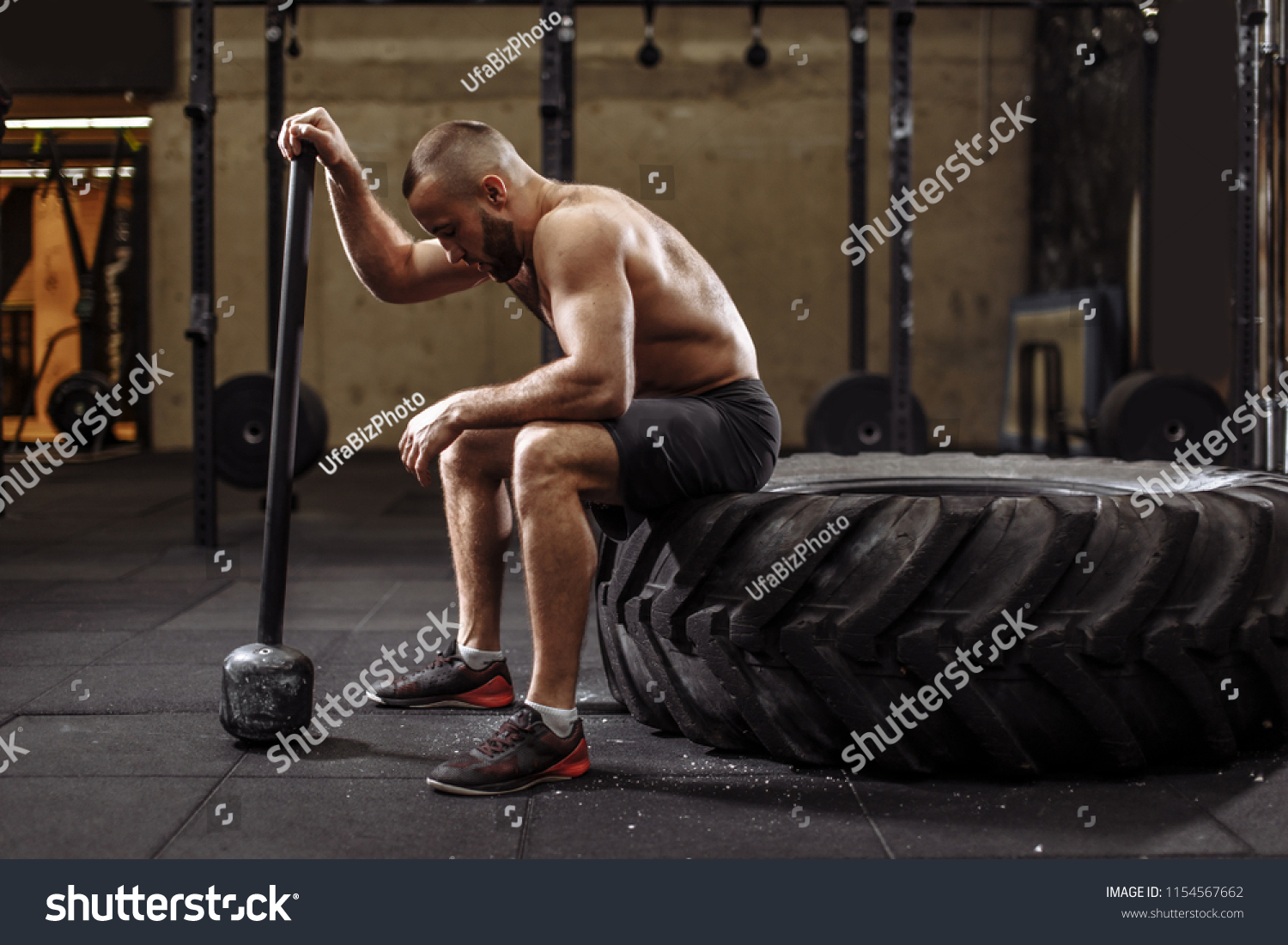handsome bodybuilder with closed eyes is resting after doing sledgehammer exercises at the gym. full length side view photo #1154567662