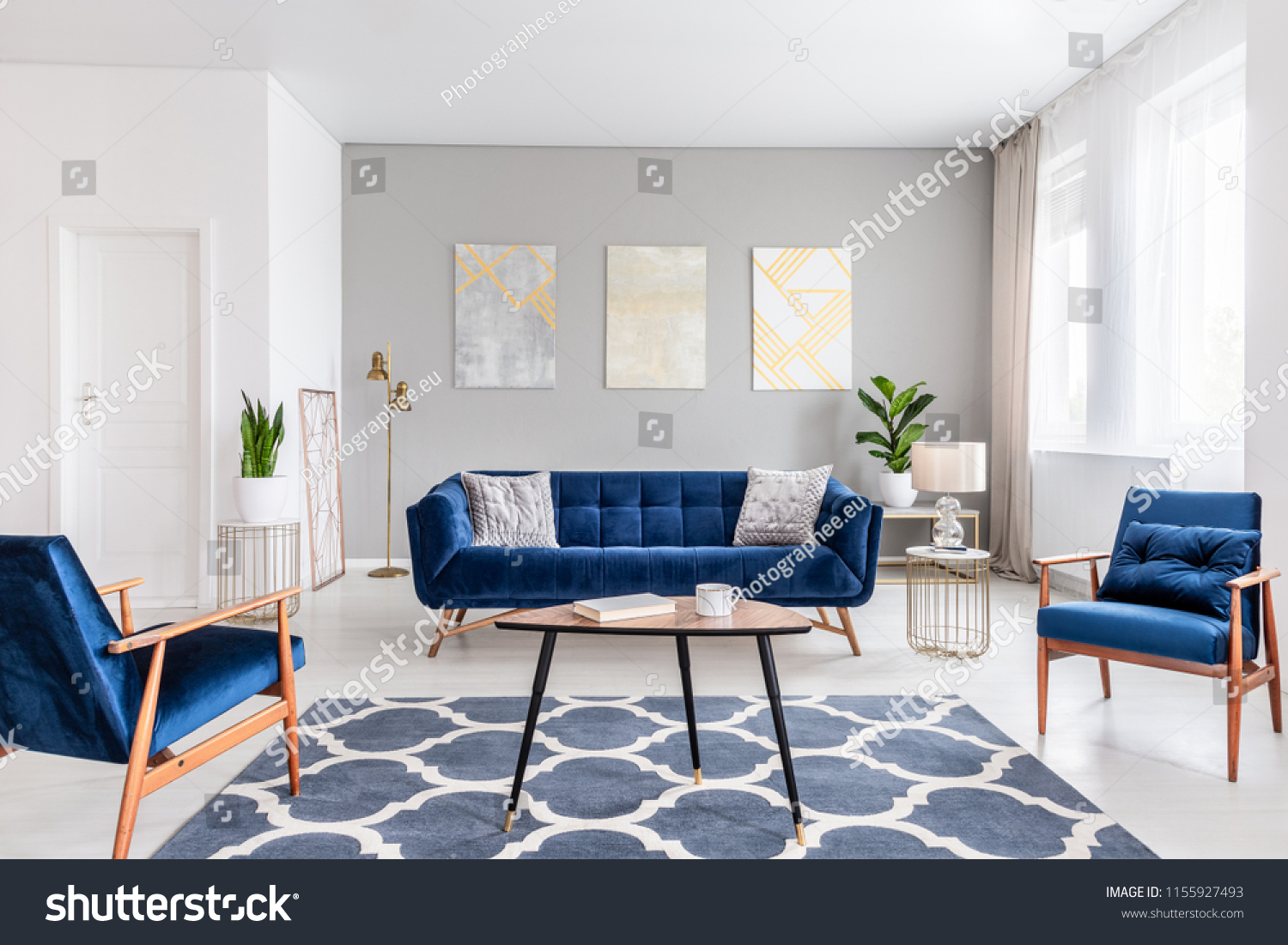 Real photo of a modern living room interior with a sofa, armchairs, table, paintings and patterned carpet #1155927493