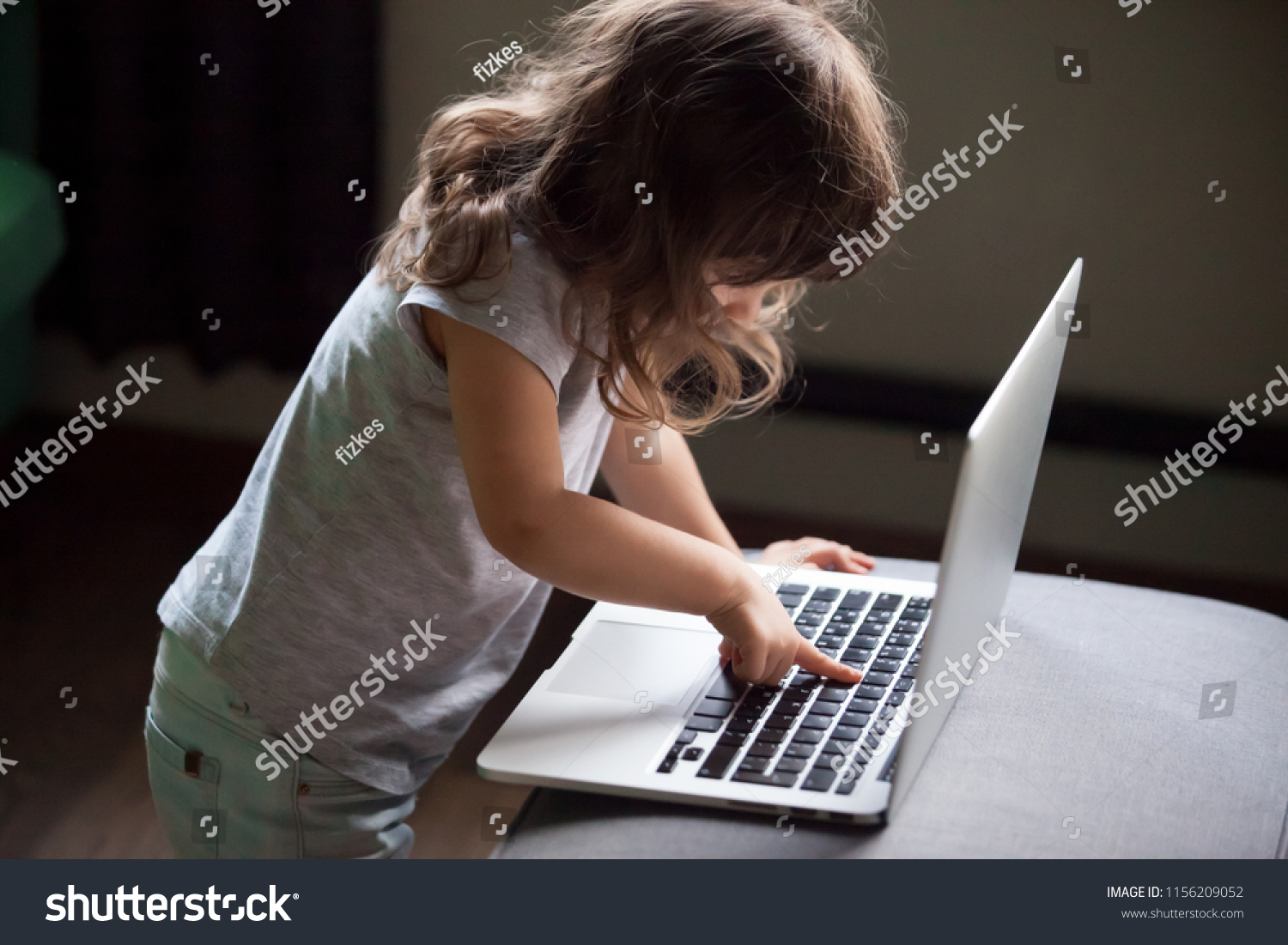 Curious smart little girl typing on laptop alone, clever cute child using computer online without permission, forbidden internet content parental protection, pc control and security for kid concept #1156209052