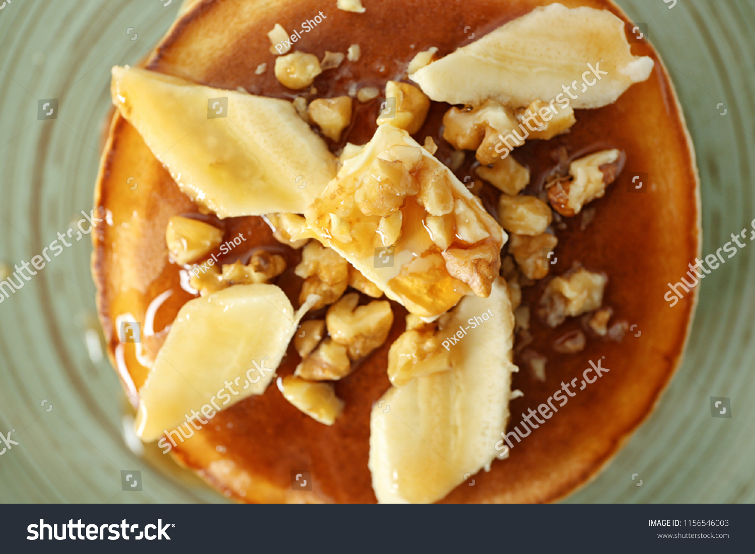 Tasty pancakes with sliced banana and walnuts on plate, closeup #1156546003