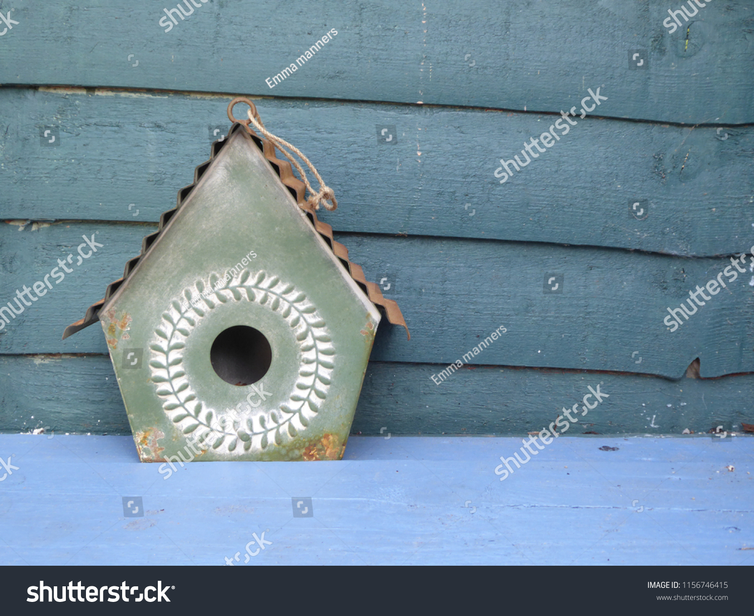 A French shabby chic style decorative green metal birdhouse on a blue wooden bench with wood panel background , a colourful garden decoration  #1156746415