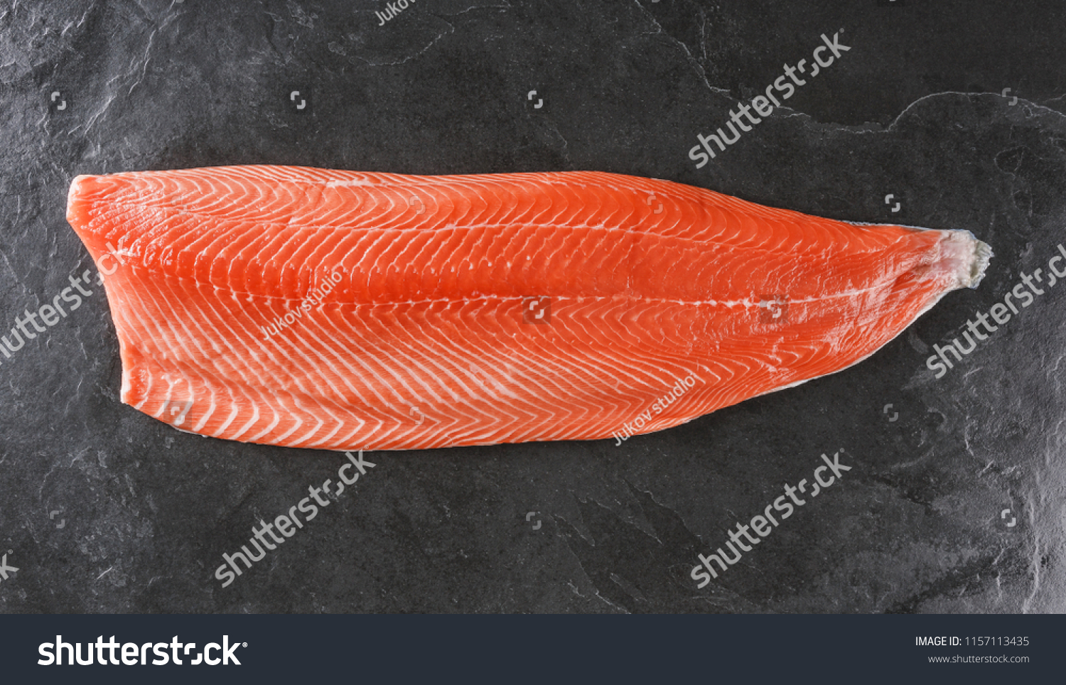 Fresh raw salmon fish steak with spices on ice over dark stone background. Creative layout made of fish, top view, flat lay #1157113435
