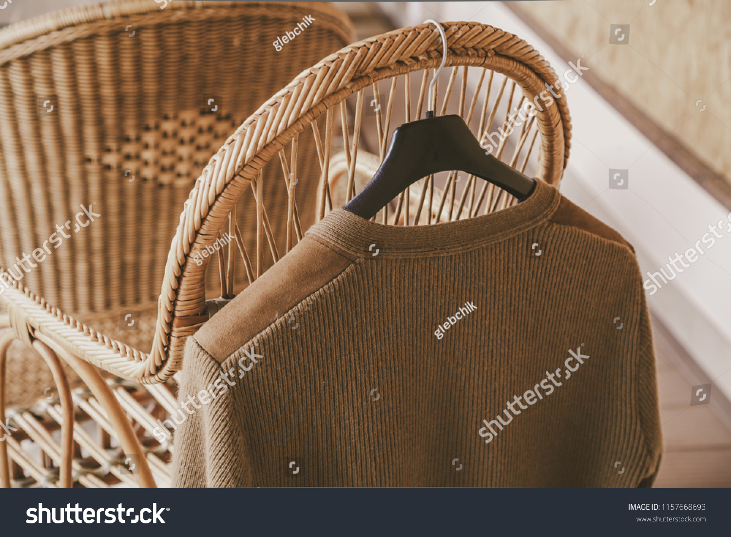 Autumn story. A woolen knitted jacket hangs on a hanger on the back of a wicker chair on the veranda
 #1157668693