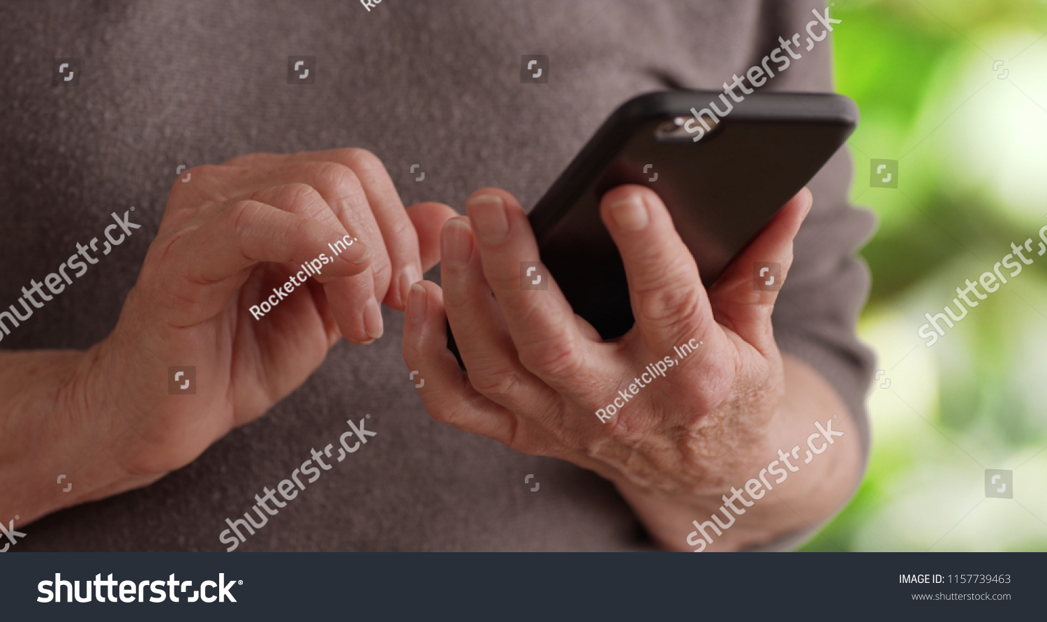 Tight shot of senior person's hands holding cell phone texting in nature setting #1157739463