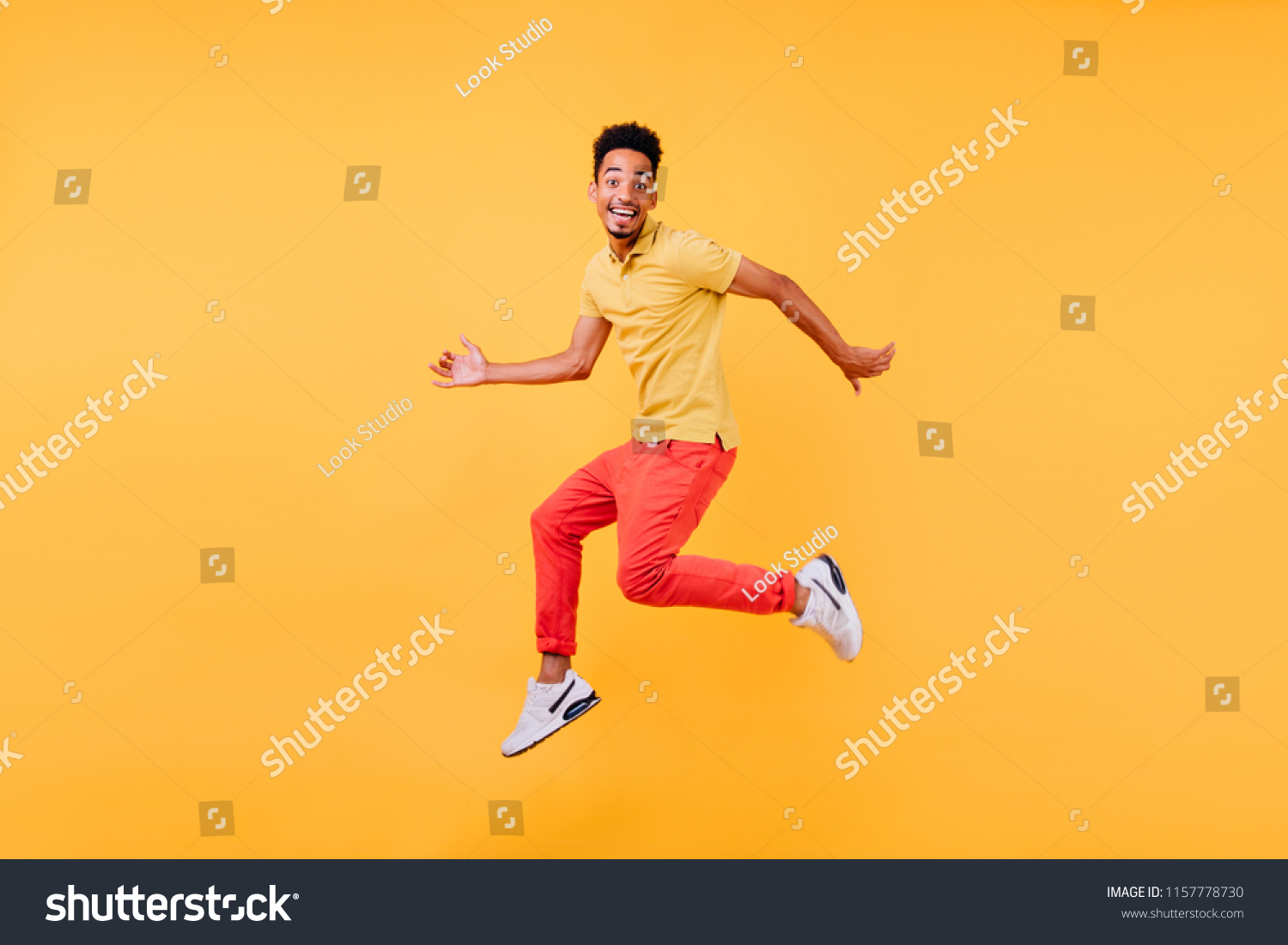 Dreamy male model. Indoor shot of african guy in bright clothes jumping on yellow background. #1157778730