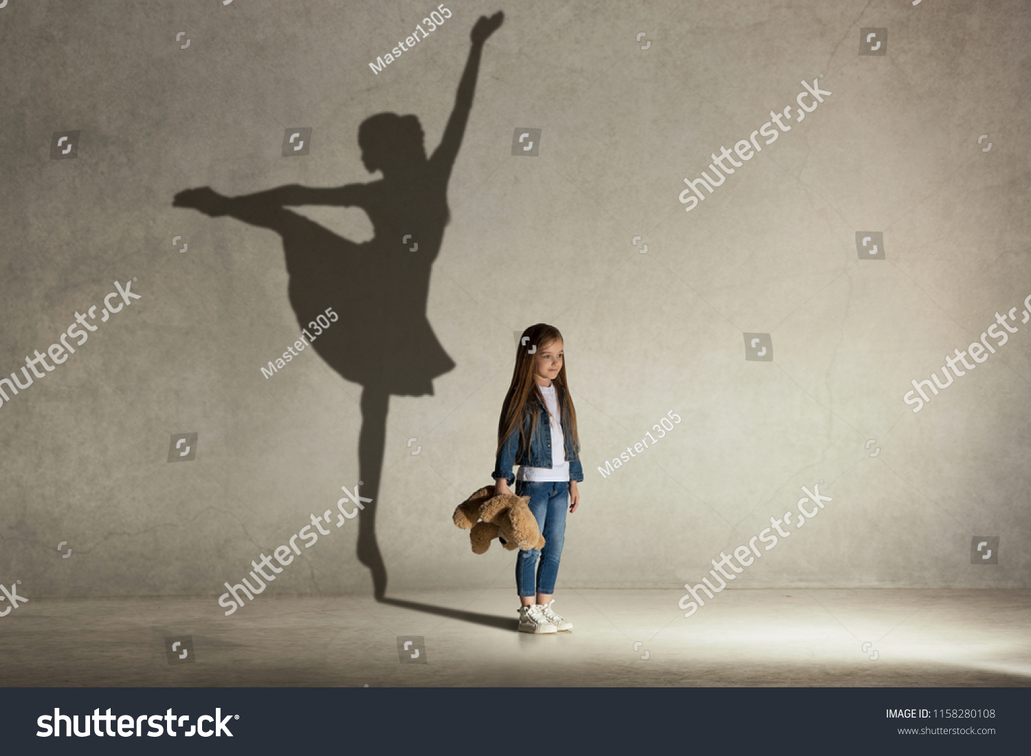Baby girl dreaming about dancing ballet. Childhood and dream concept. Conceptual image with shadow of ballerina on the studio wall #1158280108