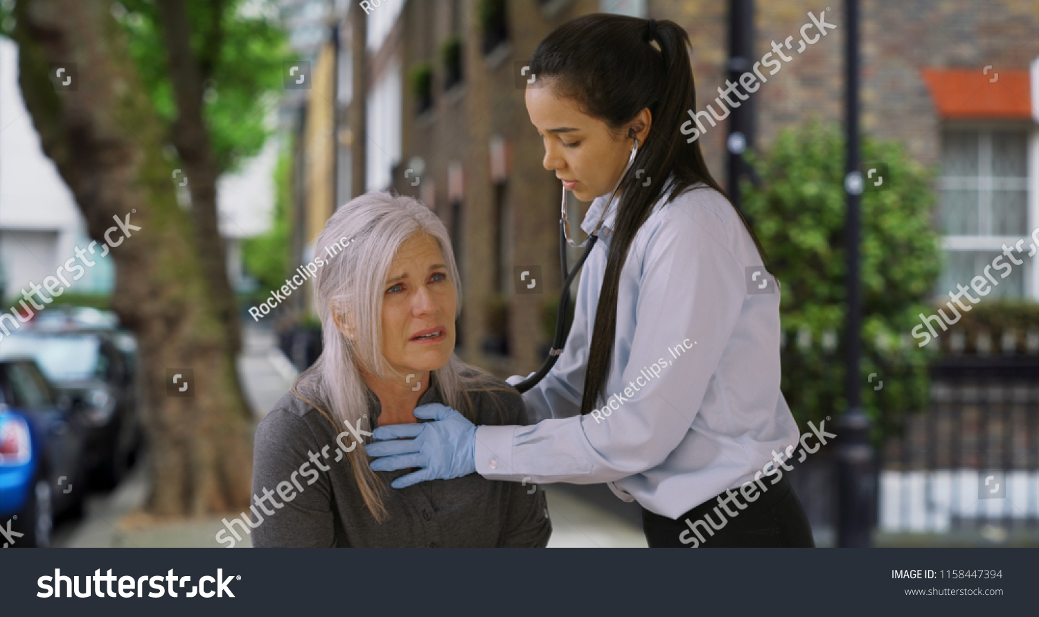 Latin woman paramedic listens to senior woman breathing on the street #1158447394