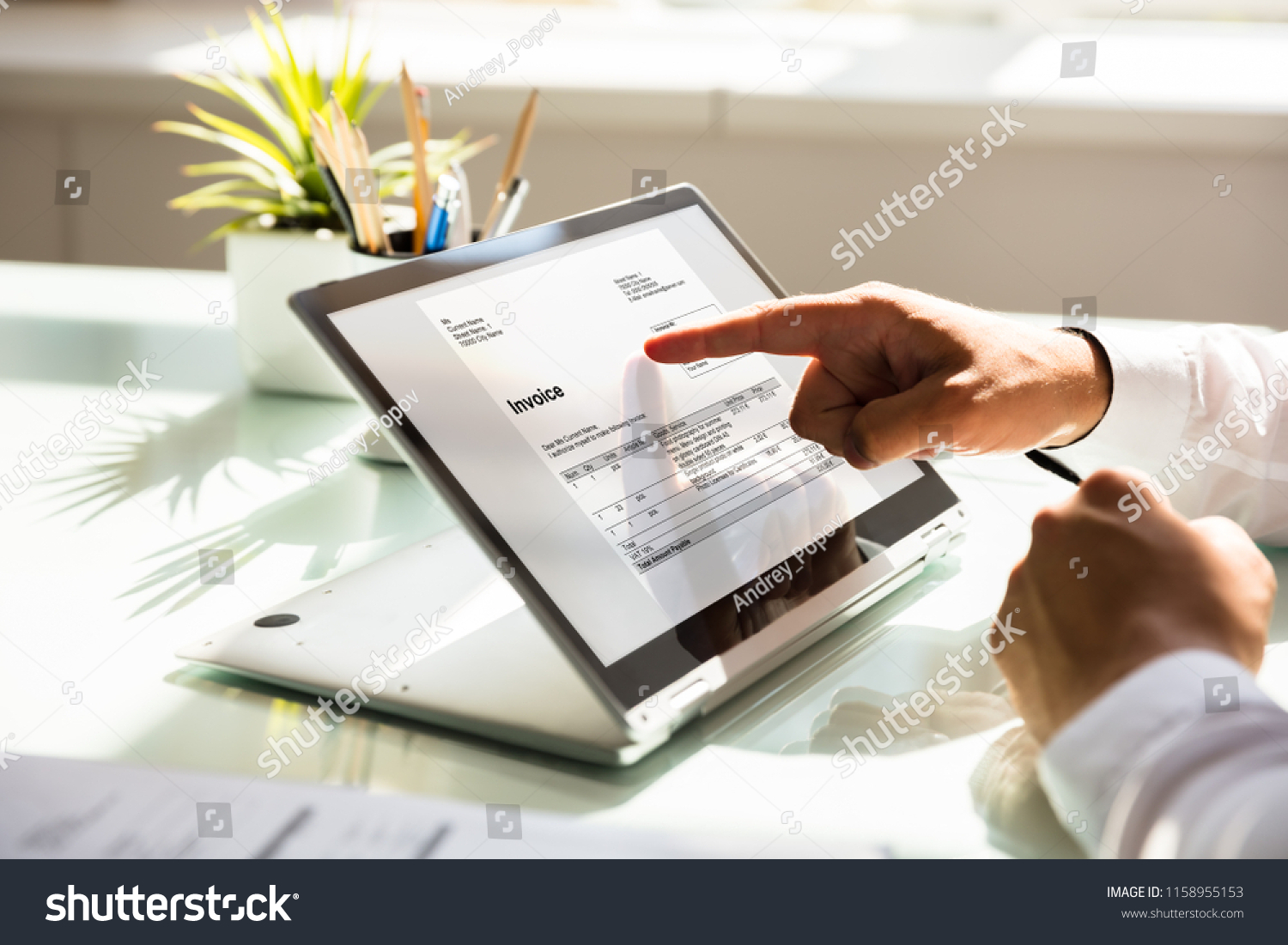 Close-up of a businessman's hand examining invoice on laptop #1158955153