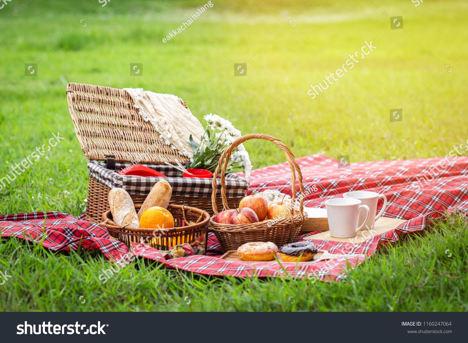 Picnic basket with fruit and bakery on red cloth in garden. #1160247064