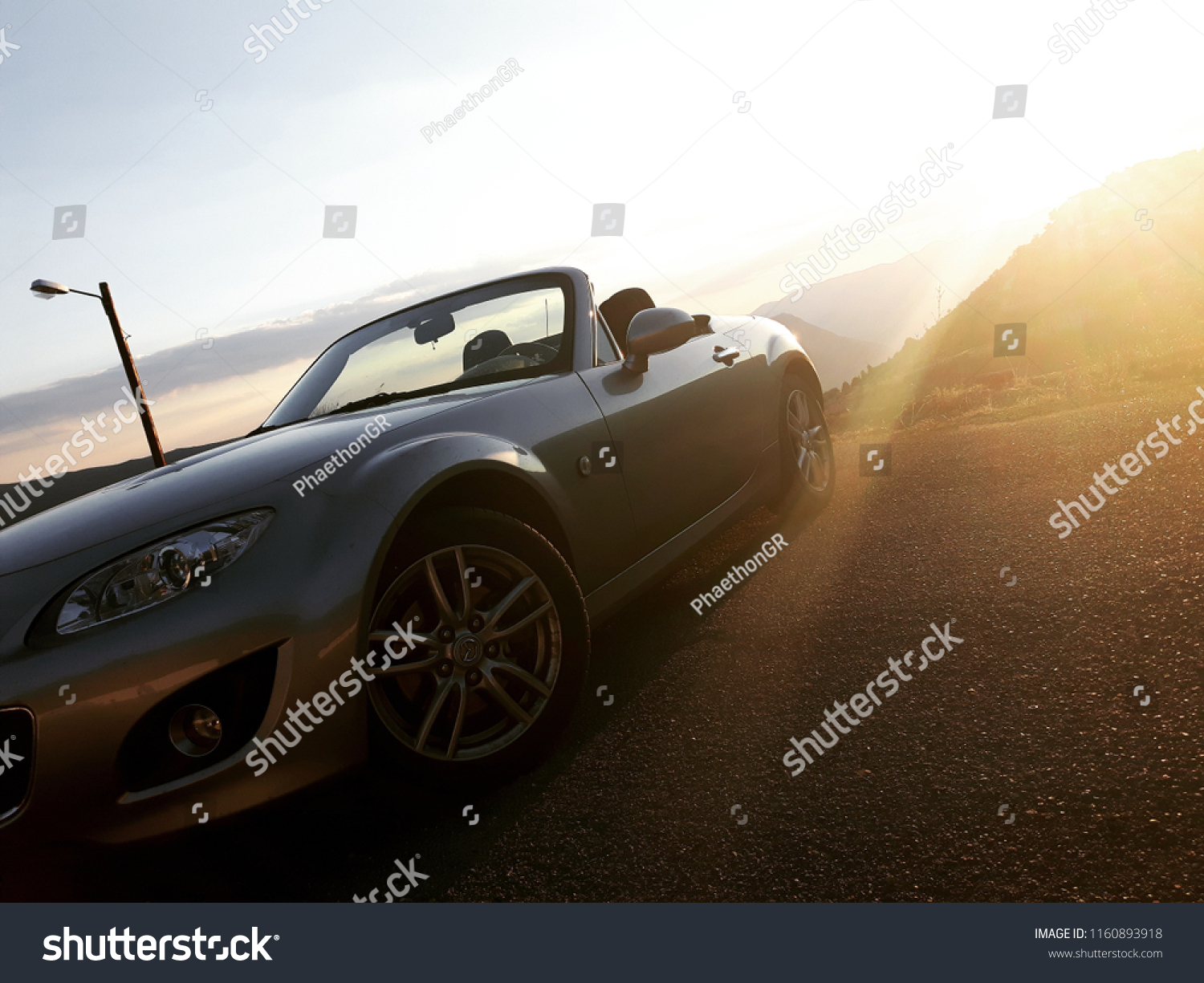 Sunset front view of silver gray convertible car, mountain valley in background #1160893918