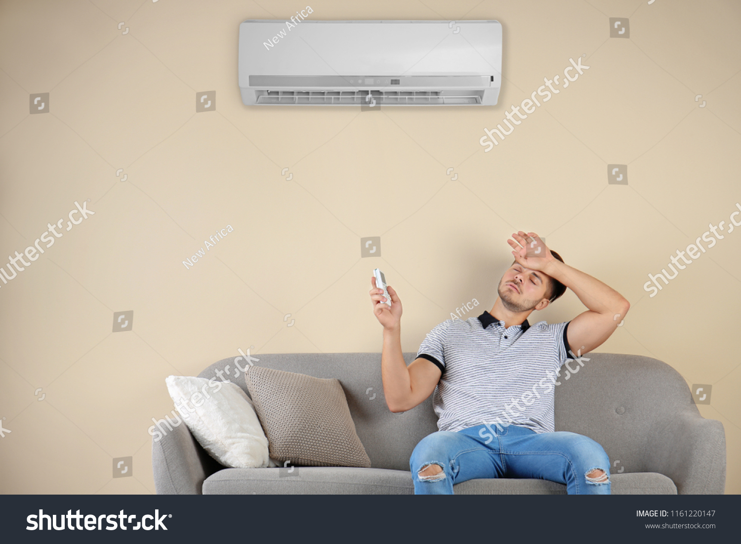 Young man operating air conditioner while sitting on sofa at home #1161220147