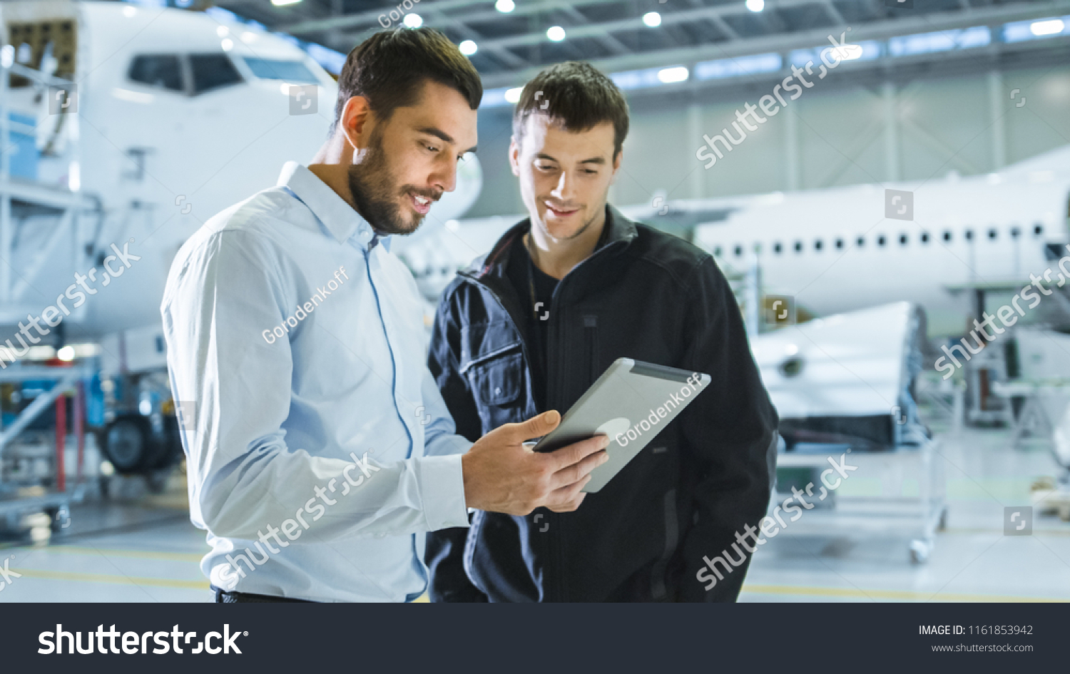 Aircraft Maintenance Worker and Engineer having Conversation. Holding Tablet. #1161853942