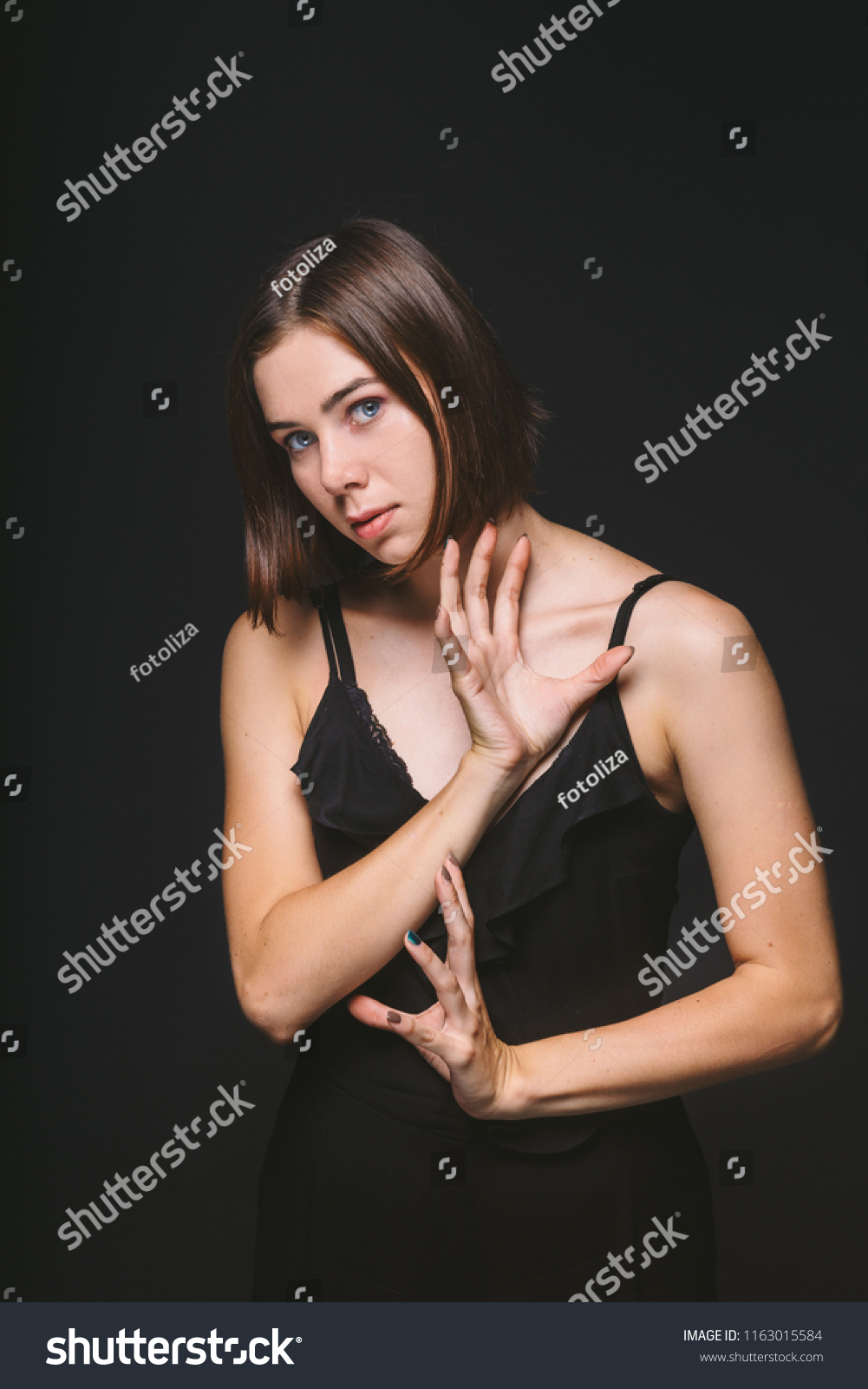 Portrait of a beautiful young Caucasian Caucasian woman 20 years old model with blue eyes natural make-up of hair on shoulder dancing hands posing on black isolated background in black lingerie. #1163015584
