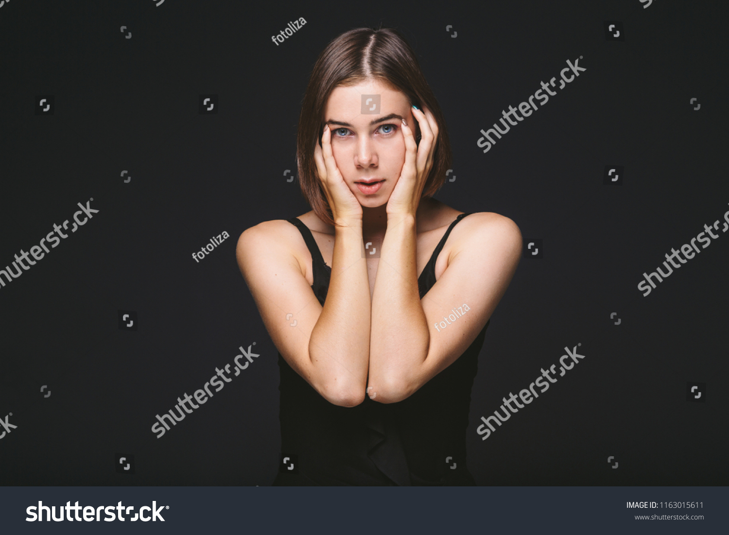 Portrait of a beautiful young Caucasian Caucasian woman 20 years old model with blue eyes natural make-up of hair on shoulder dancing hands posing on black isolated background in black lingerie. #1163015611