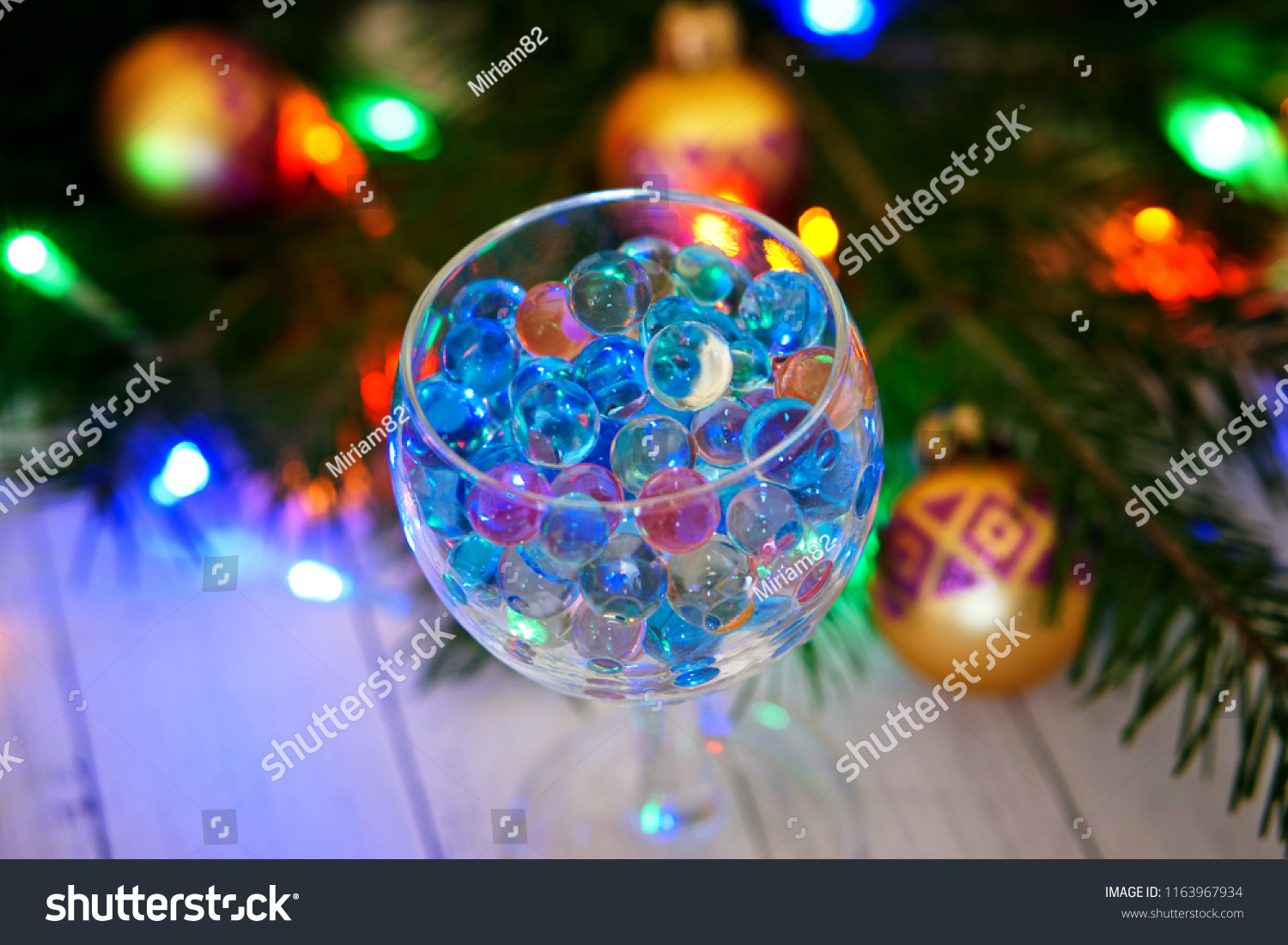 Transparent glass with gel balls on the background of a Christmas tree. An unusual drink.                                #1163967934