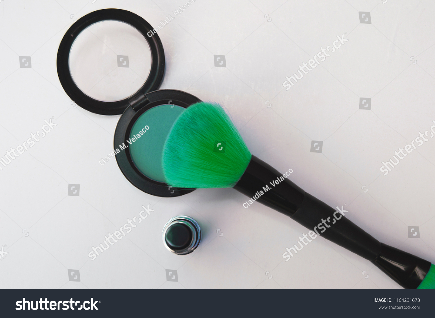 Areal view of a delicate green eye shadow and a soft, fluffy makeup brush over a white background. Beauty products concept #1164231673