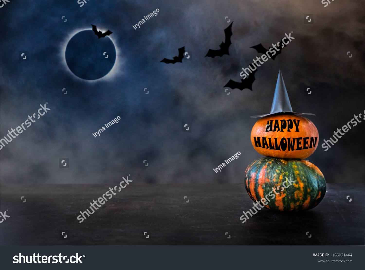 Two pumpkins with witch hat and text HAPPY HALLOWEEN against the background of the night sky, bats and the moon eclipse. Pumpkins At Moonlight In The Spooky Night - Halloween Scene #1165021444
