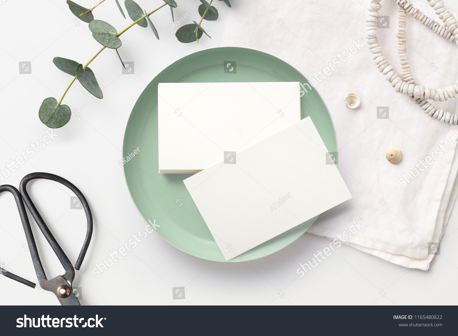 stack of blank business cards on a white feminine styled desk with mint bowl, decorative scissors, linen napkin and eucalyptus twigs. minimalist mock up, flat lay / top view #1165480822