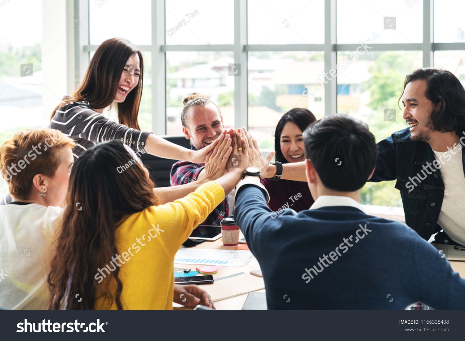 group of young multiethnic diverse people gesture hand high five, laughing and smiling together in brainstorm meeting at office. Casual business with startup teamwork community celebration concept. #1166338408