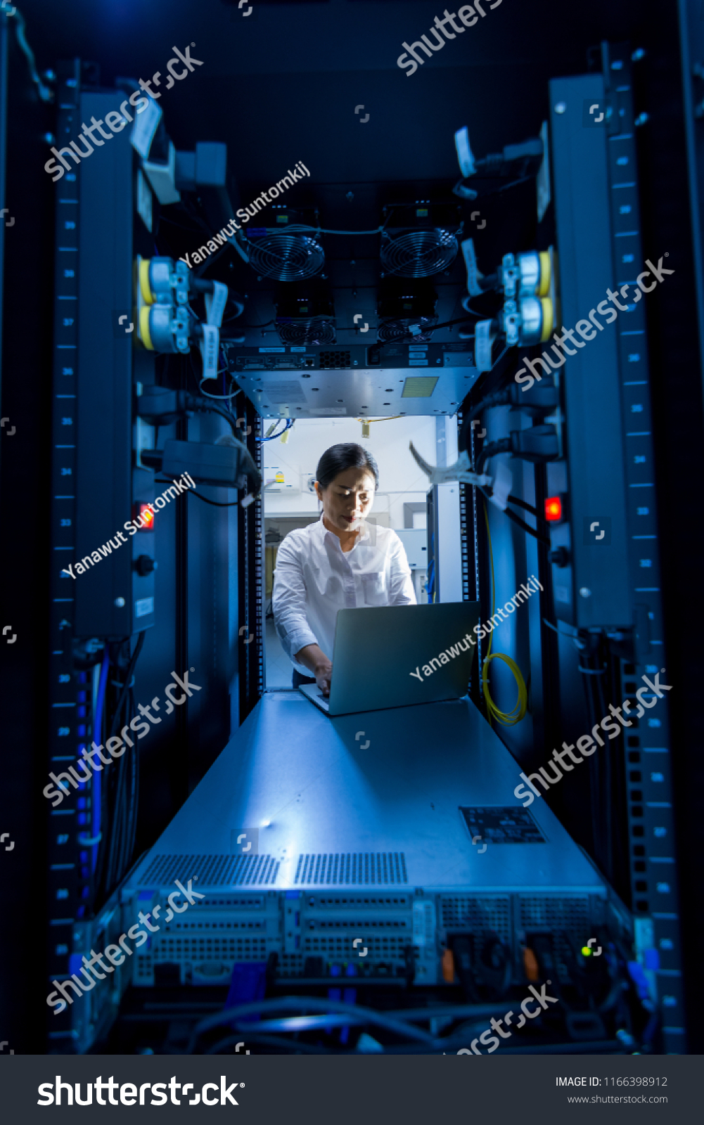 Asian female network administrator using laptop computer at networking rack cabinet on working in data center room #1166398912
