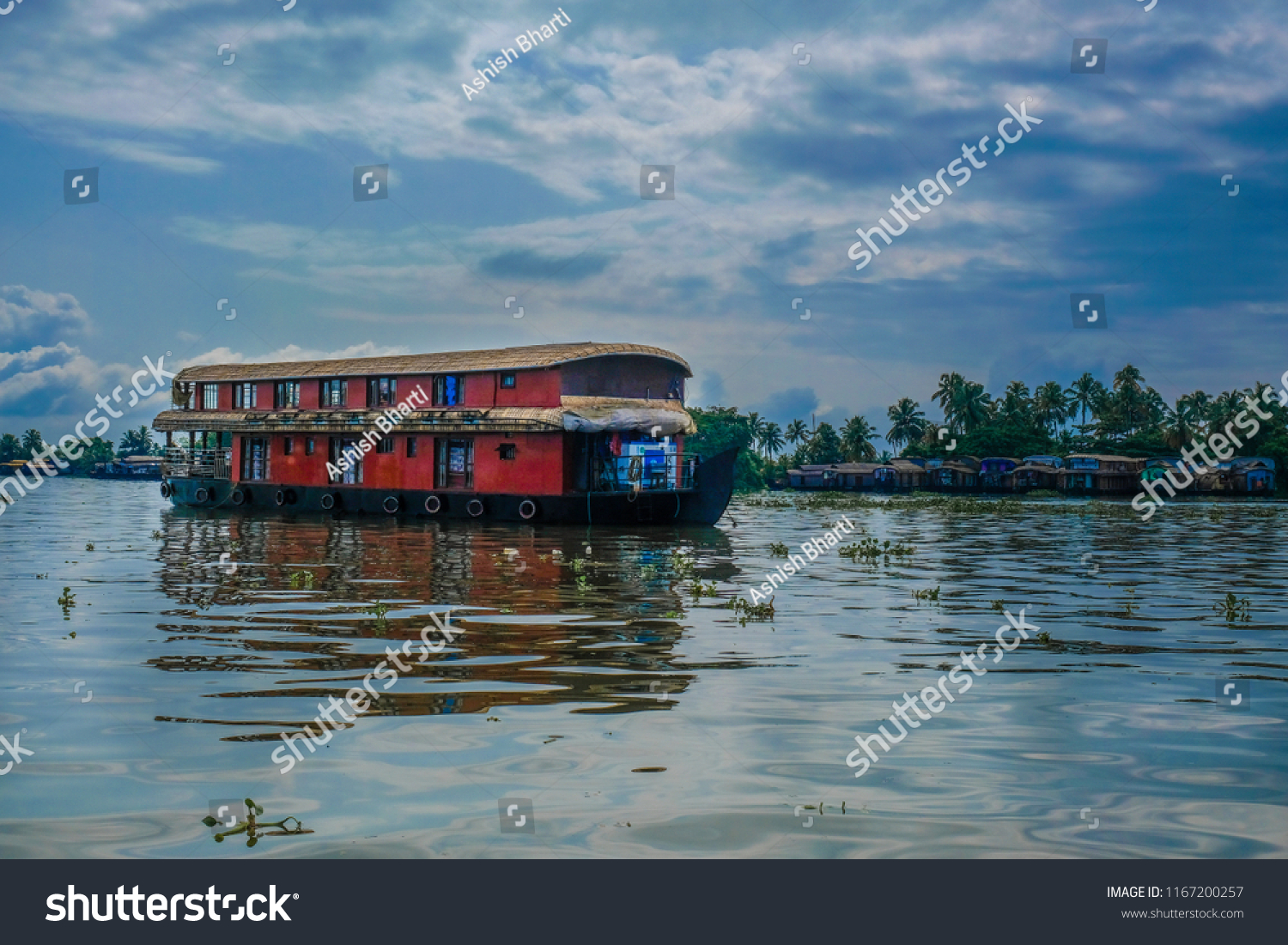 A boathouse in backwaters of Alleppey in Kerala, India with blue sky and clouds with reflection in water #1167200257