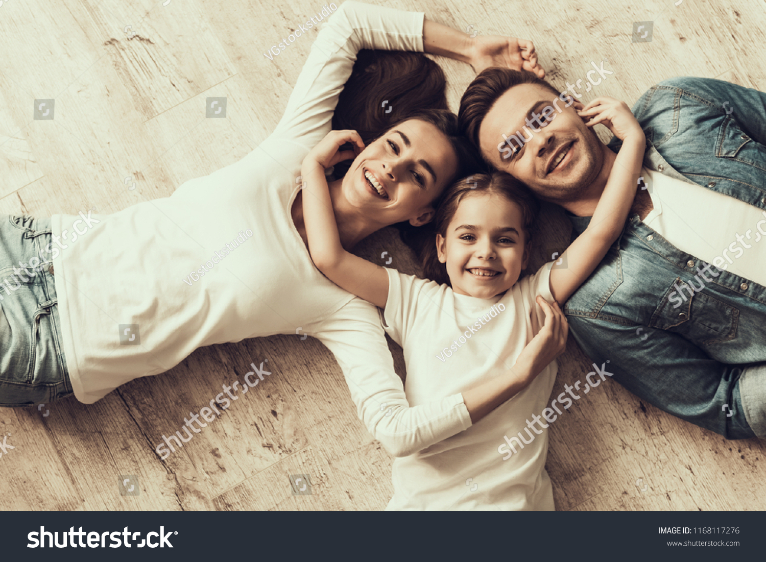 Happy Family Lying of Floor Together at Home. Beautiful Woman Handsome Man and Adorable Little Girl Lying on Parquet Floor and Hugging. Parents and Child Together. Family and Parenthood Concept #1168117276