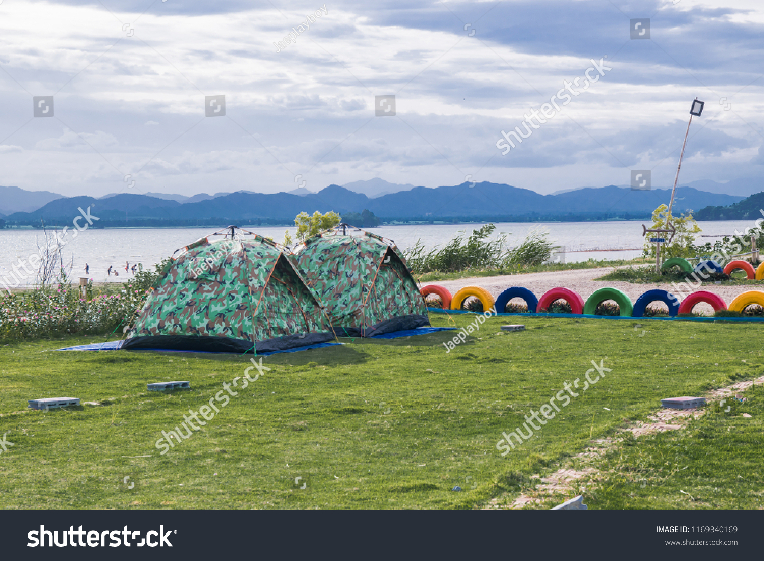 A couple tent is camping on the green grass field  near the river with blue sky and mountain #1169340169