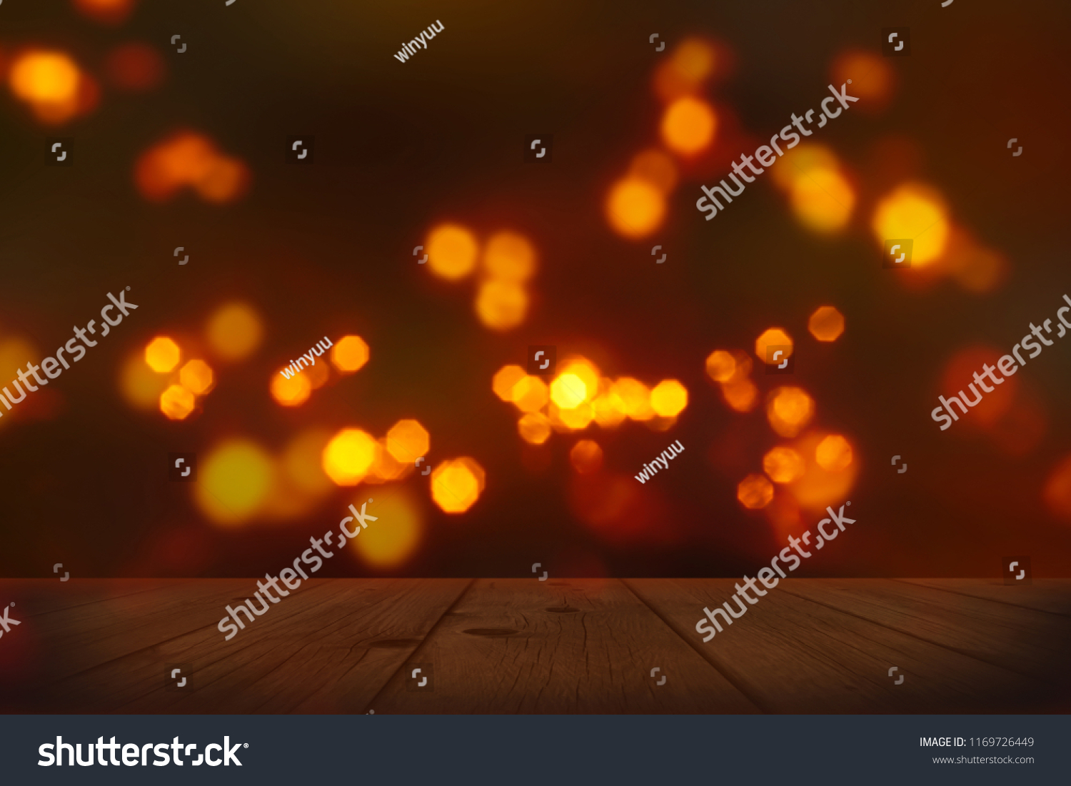 festive background with blurry lights, empty wooden table in foreground with bright candlelight bokeh on dark blurred backdrop, celebration at night concept #1169726449