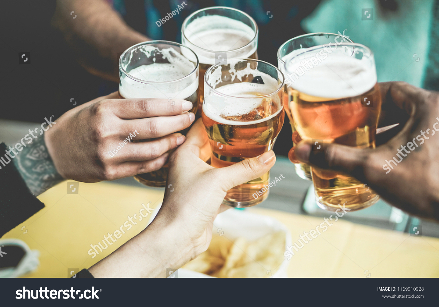 Group of friends enjoying a beer in brewery pub - Young people hands cheering at bar restaurant - Friendship and youth concept - Main focus on left bottom hands #1169910928