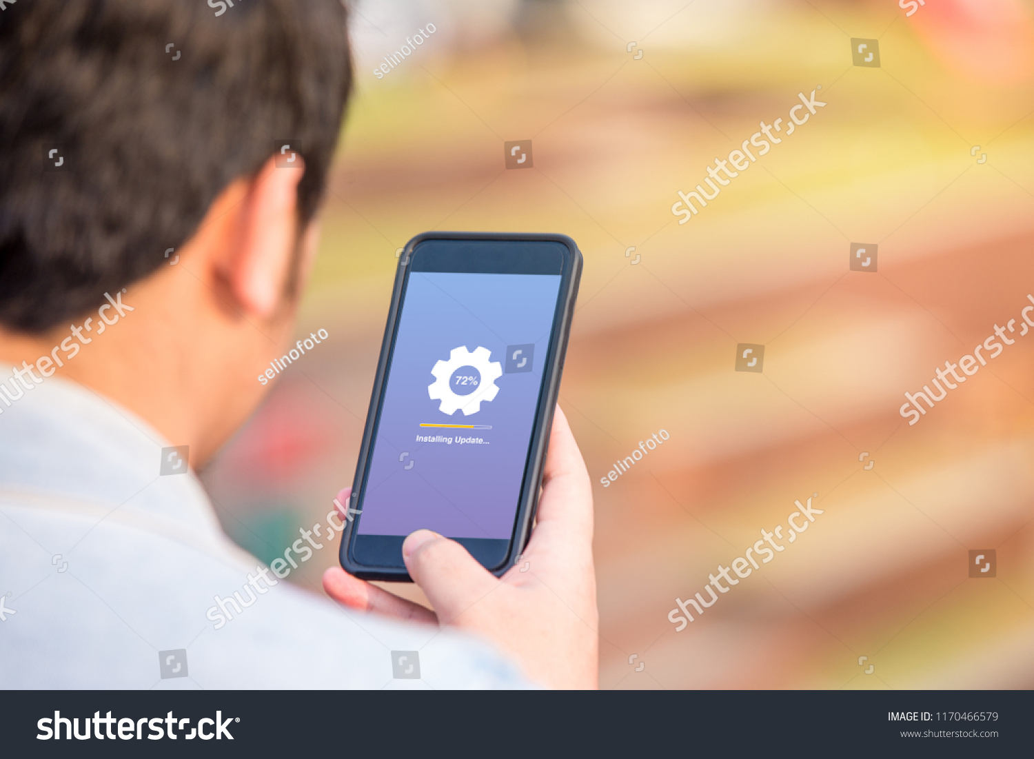 Installing update concept on phone screen. Man holding phone doing installing update process with gearbox percentage progress and loading bar. #1170466579