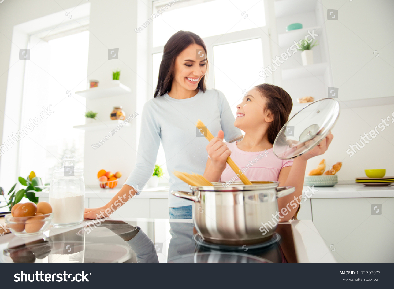 Charming adorable attractive beautiful caucasian kind young smiling mum and her small little offspring daughter having fun, praparing vermicelli in light kitchen #1171797073
