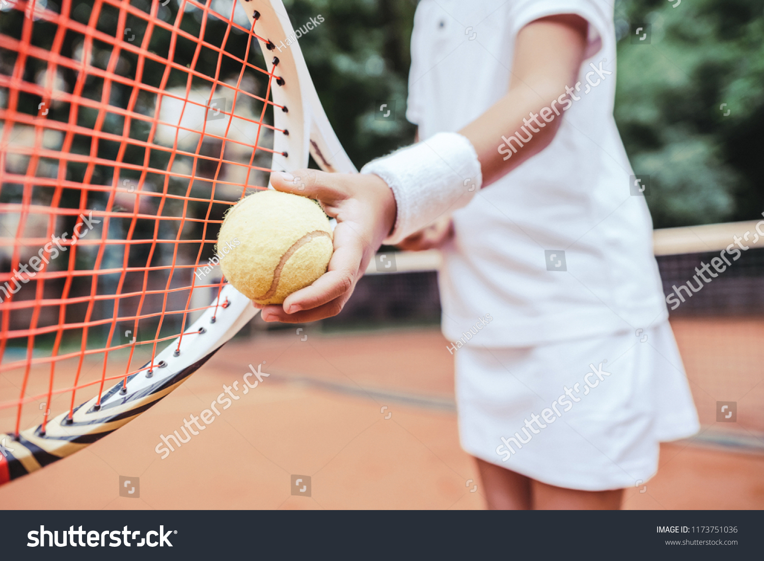 Sporty little girl preparing to serve tennis ball. Close up view of beautiful yong girl holding tennis ball and racket. Child tennis player preparing to serve. #1173751036