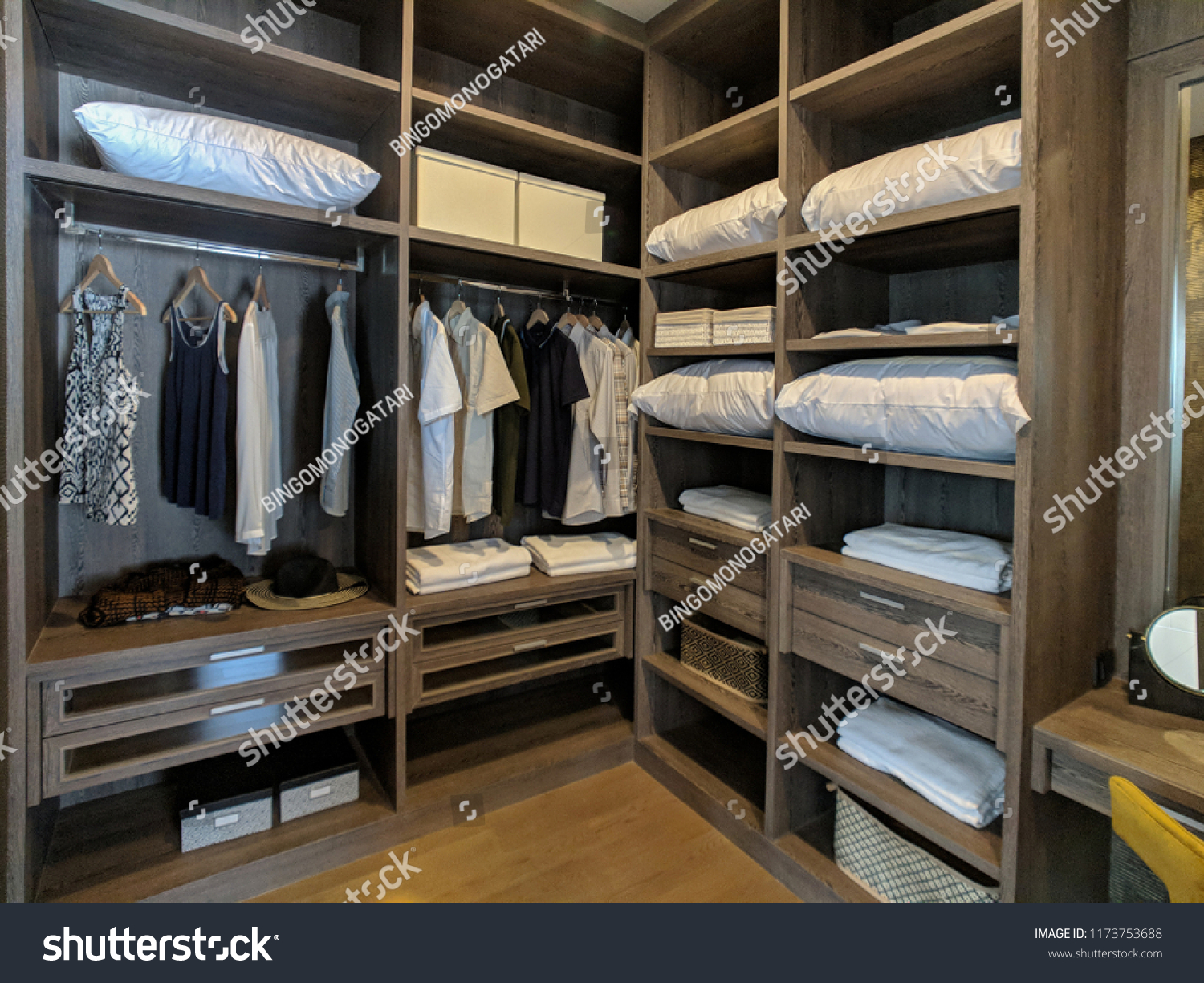 Walk in closet with wooden shelves There are pillows and hanging clothes. #1173753688