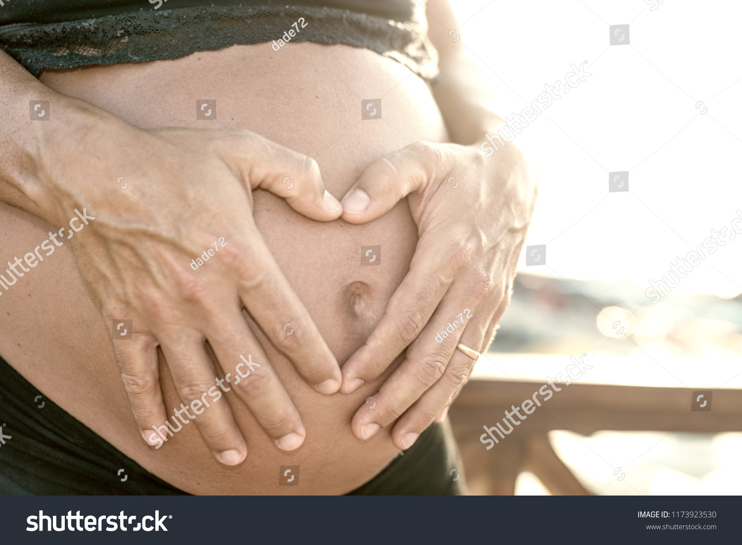 Pregnant woman on the beach - hands of the husband in heart shape on belly. #1173923530