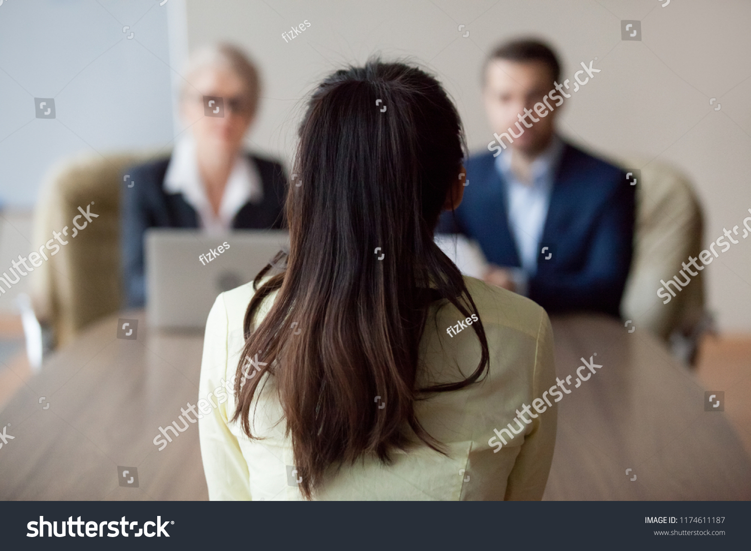 Businesswoman and businessman HR manager interviewing woman. Candidate female sitting her back to camera, focus on her, close up rear view, interviewers on background. Human resources, hiring concept #1174611187
