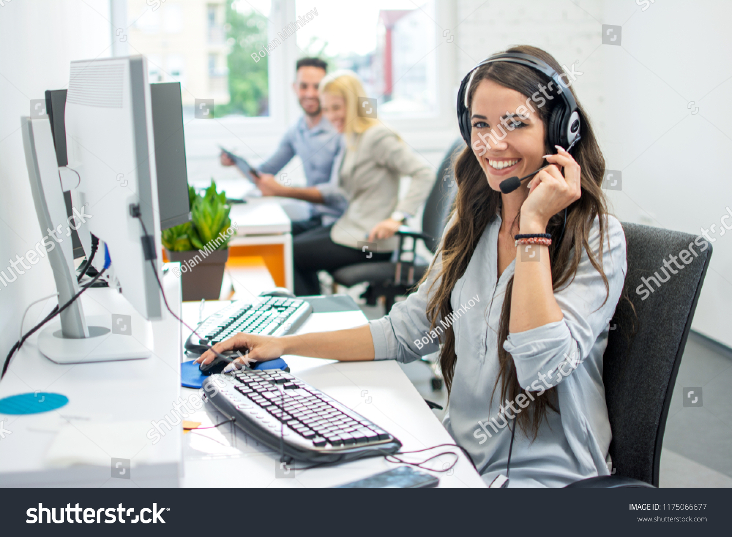 Smiling friendly female call-center agent with headset working on support hotline in the office #1175066677