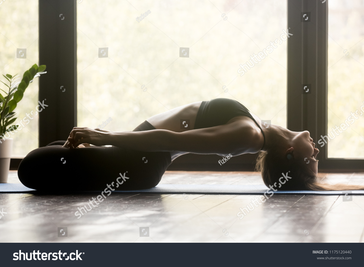 Young sporty woman practicing yoga, doing variation of Matsyasana with lotus legs exercise, Fish pose, working out, wearing sportswear, grey pants and top, indoor full length, yoga studio #1175120440