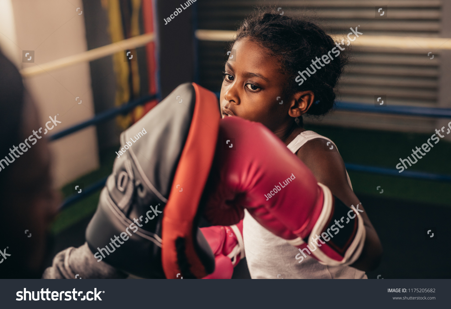 Close up of a kid training inside a boxing ring. Kid boxer wearing boxing gloves practicing punches on a punching pad. #1175205682